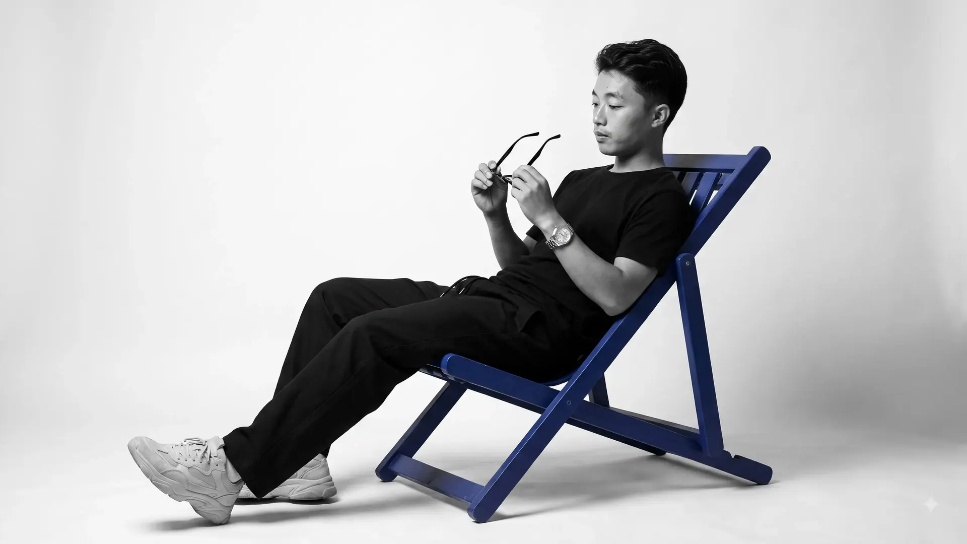 Paikhomba Wahengbam reclining in a blue folding deck chair in a black-and-white studio portrait